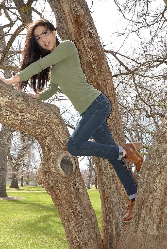 Latina chick Bella Quinn climbs a tree in the park wearing a sweater and jeans