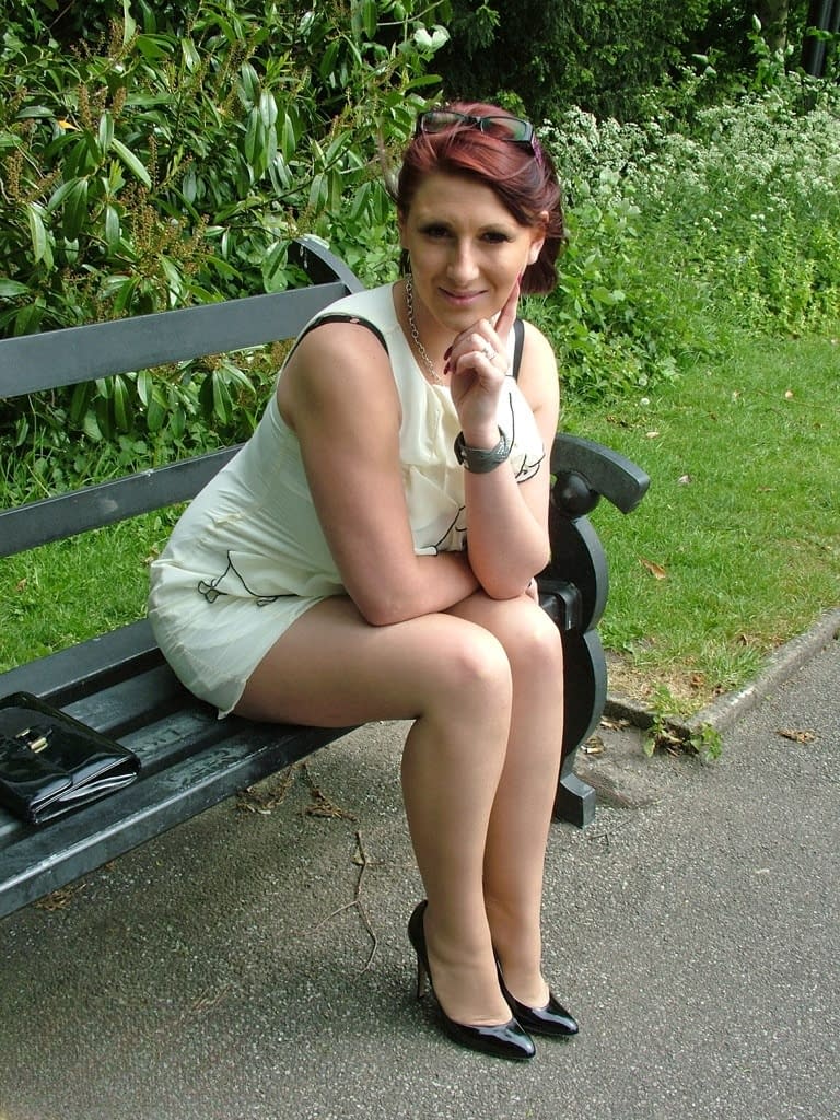 Thick woman in glasses shows off her stiletto heels on a park bench