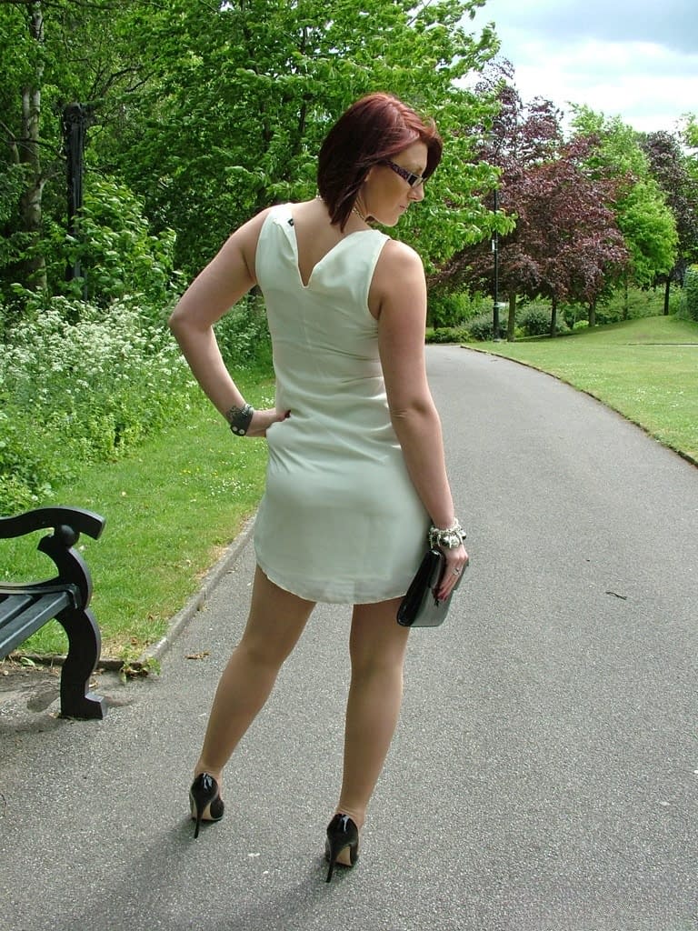 Thick woman in glasses shows off her stiletto heels on a park bench