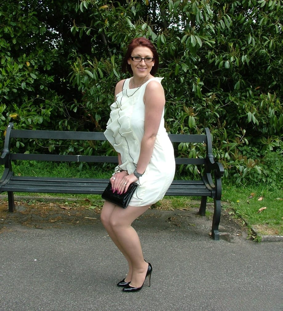 Thick woman in glasses shows off her stiletto heels on a park bench