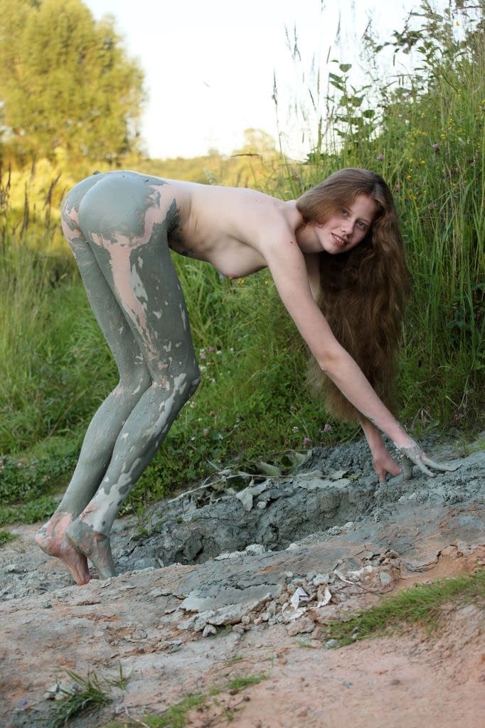 Naked teen girl with long legs covers herself in mud from head to toes