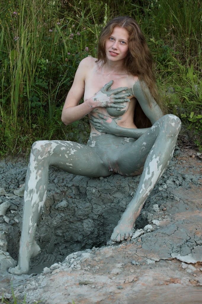 Naked teen girl with long legs covers herself in mud from head to toes
