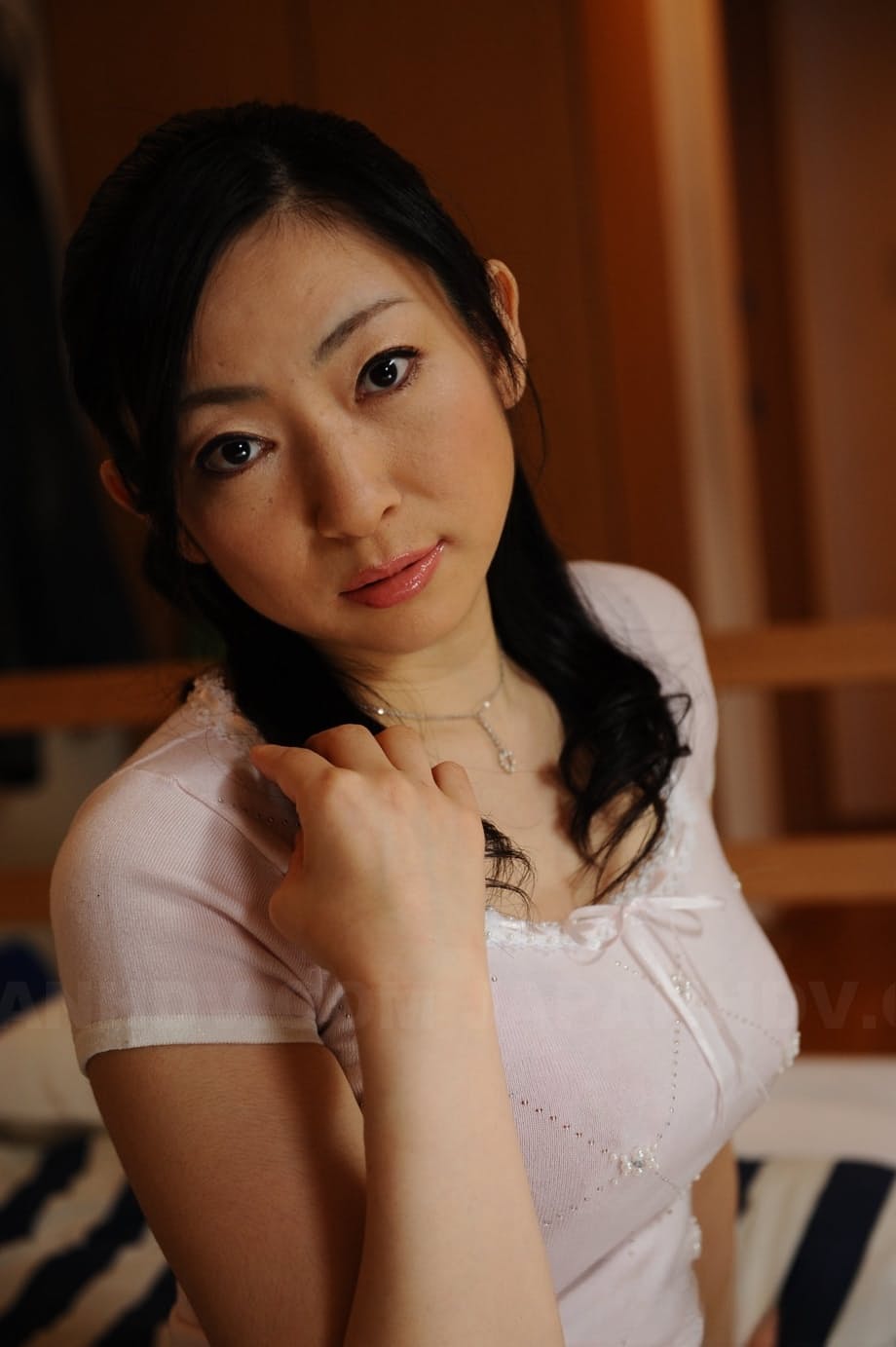 Slender mature Japanese woman Emiko Koike bends over to pose in white dress