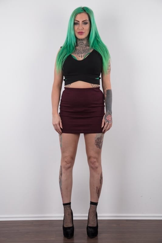 Tattooed girl with green hair and pierced nipples stands naked after disrobing