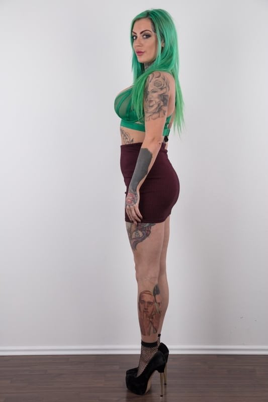 Tattooed girl with green hair and pierced nipples stands naked after disrobing