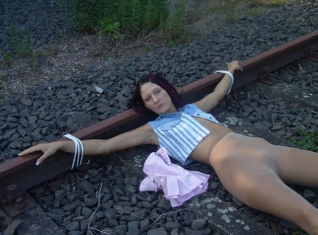 Brunette girl has her hose pulled down after being tied to train tracks