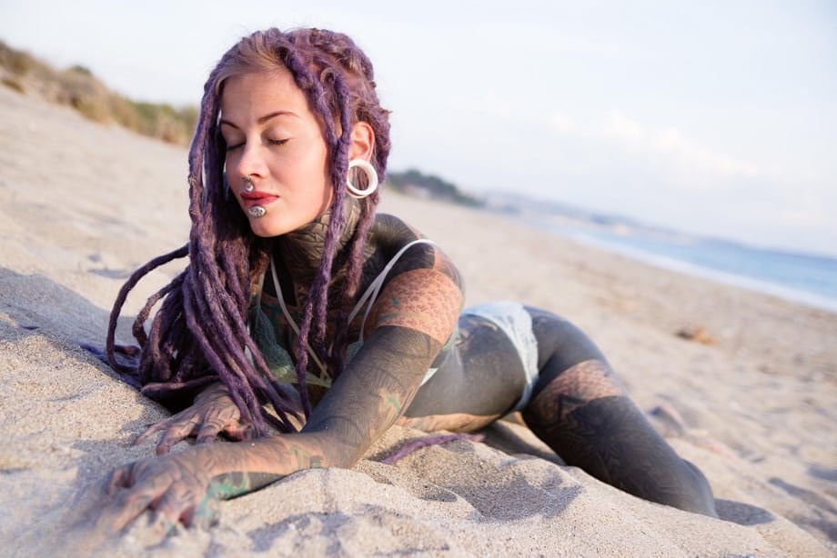 Heavily tattooed girl releases tiny tits from bikini top on a sandy beach
