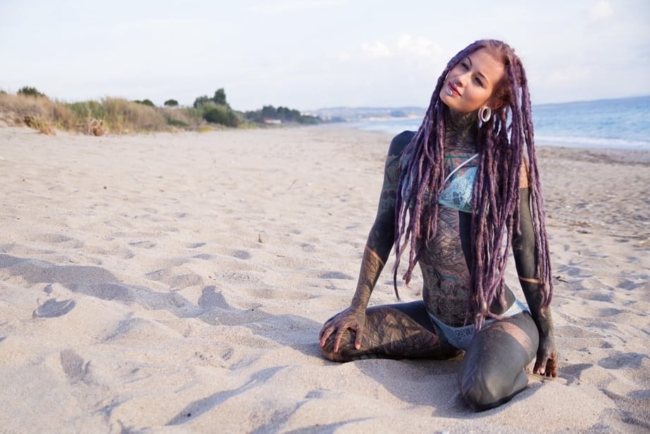 Heavily tattooed girl releases tiny tits from bikini top on a sandy beach