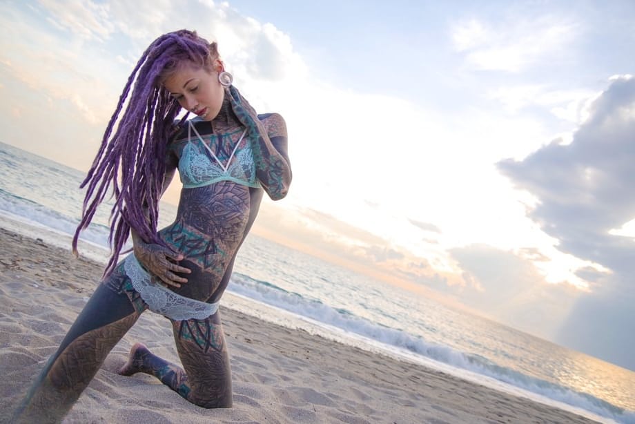 Heavily tattooed girl releases tiny tits from bikini top on a sandy beach