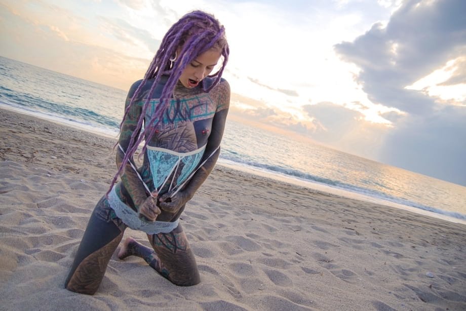 Heavily tattooed girl releases tiny tits from bikini top on a sandy beach