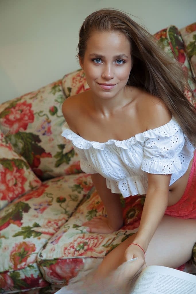 Nice teen Cassia flips thru a book before posing naked on a chesterfield