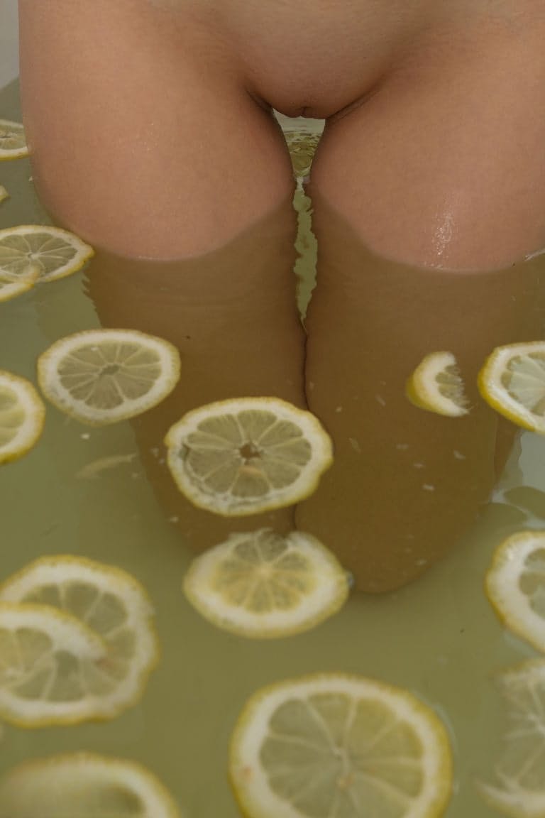 Cute blonde teen sinks her bald twat into a tub filled with lemon slices