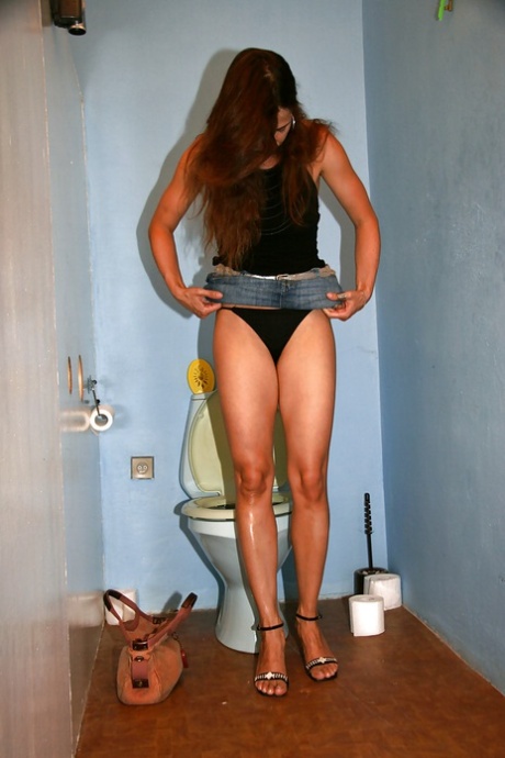 Attractive long-haired babe sits on toilet bowl and masturbates