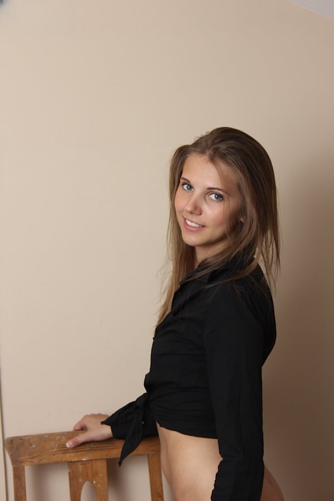 Teen with skinny shape Kira is sitting on the chair with spread legs