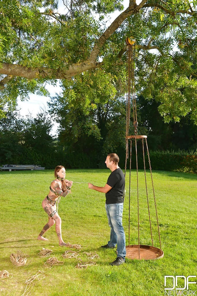 Inked fetish model undergoing outdoors slave training in collar