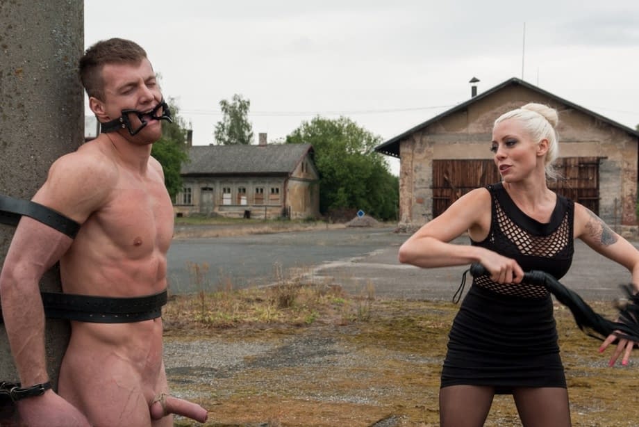 Blonde domme Lorelei Lee whips her helpless slave tied to a pole outdoors