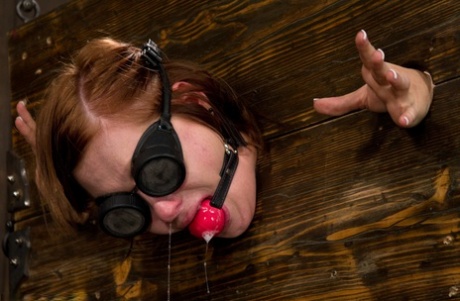 Gagged slave Charlie Ann cuffed in the pillory for naked BDSM ass whipping