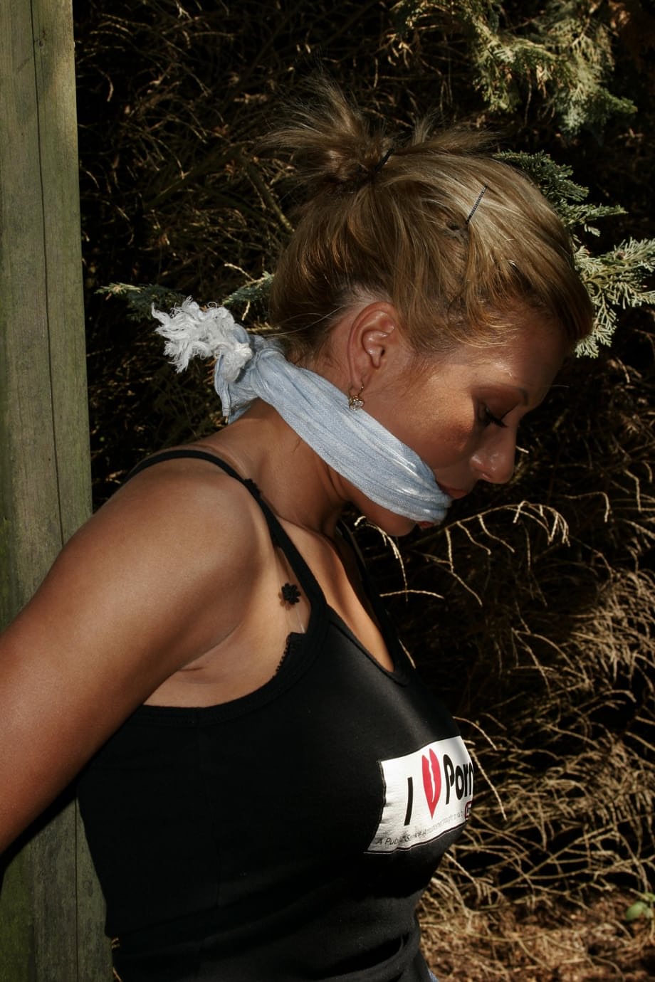 Blonde chick is left bound and gagged to a wooden structure in the woods