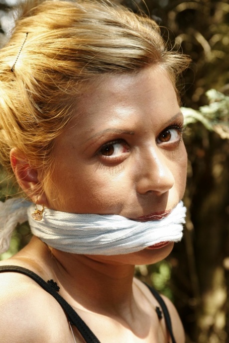 Blonde chick is left bound and gagged to a wooden structure in the woods