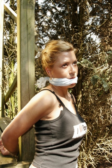 Blonde chick is left bound and gagged to a wooden structure in the woods
