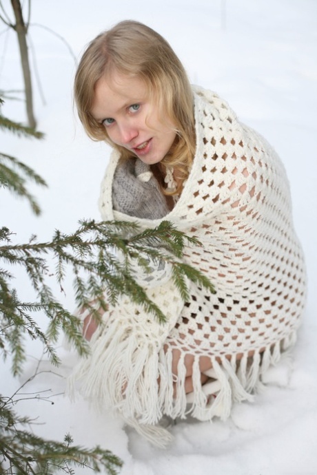 Sexy blonde girl poses nude in a snowy forest wearing gloves and boots