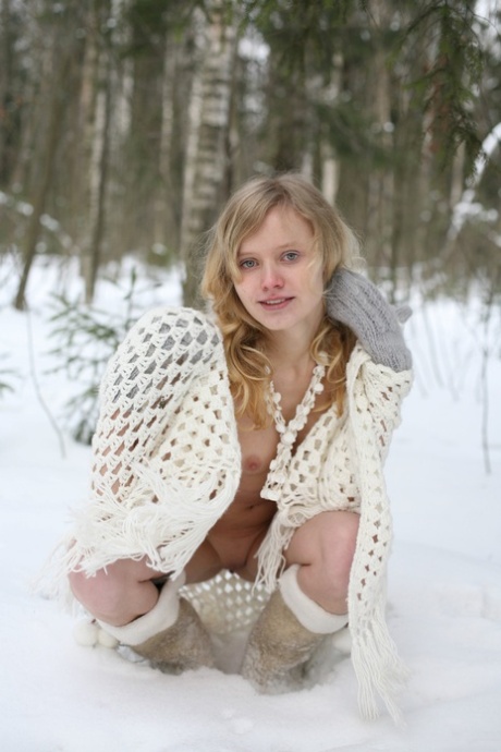Sexy blonde girl poses nude in a snowy forest wearing gloves and boots