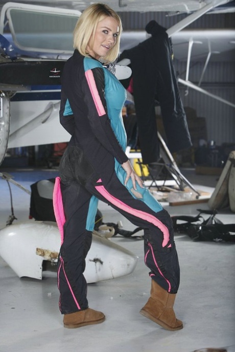 Blonde chick unzips her jumpsuit for nude poses inside an aircraft hangar