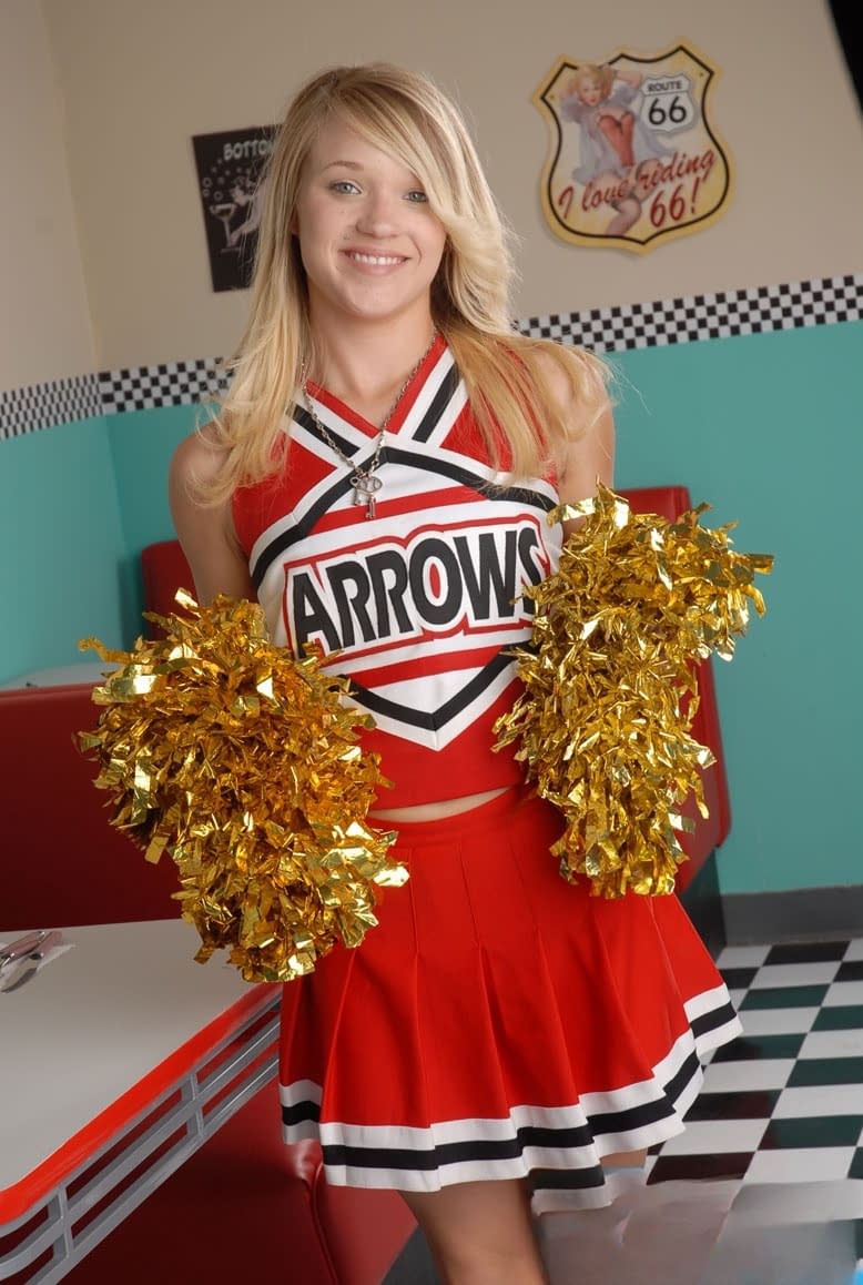 Cute college blonde Tegan Summers poses in a cheerleader outfit at a diner