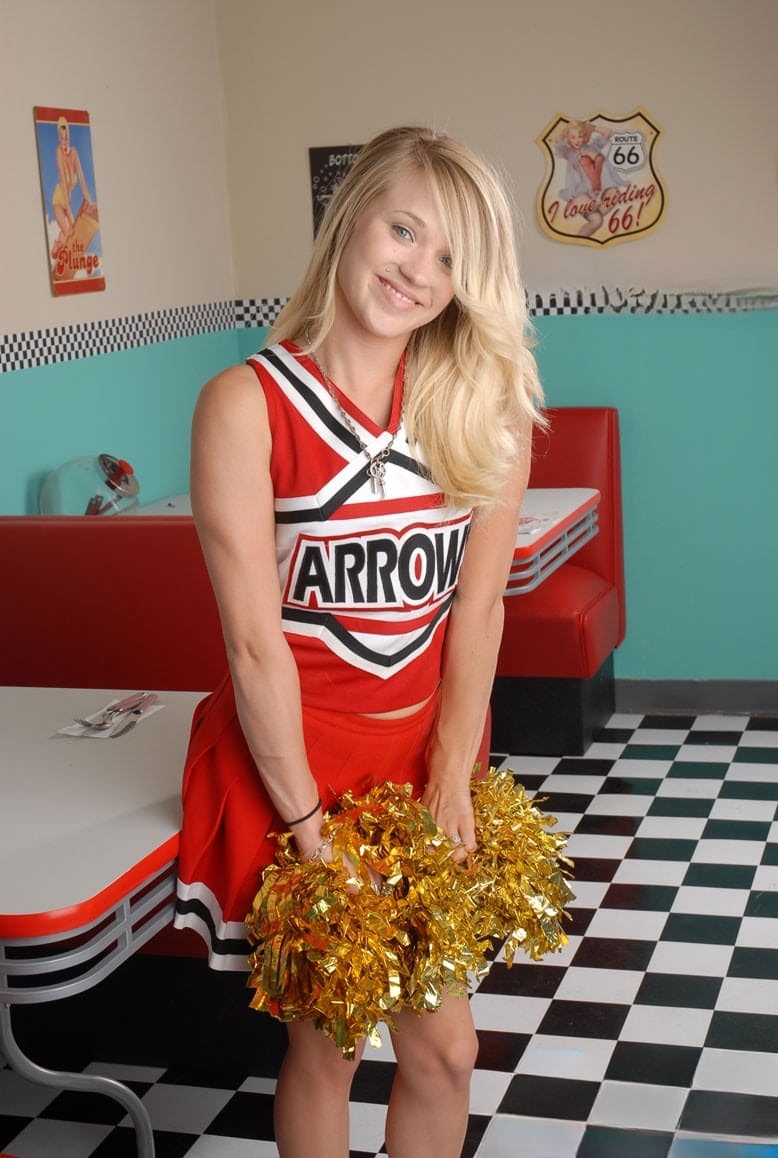 Cute college blonde Tegan Summers poses in a cheerleader outfit at a diner