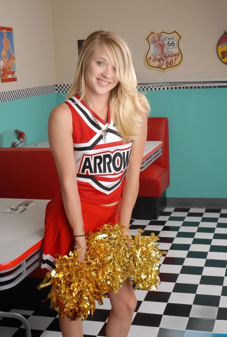 Cute college blonde Tegan Summers poses in a cheerleader outfit at a diner