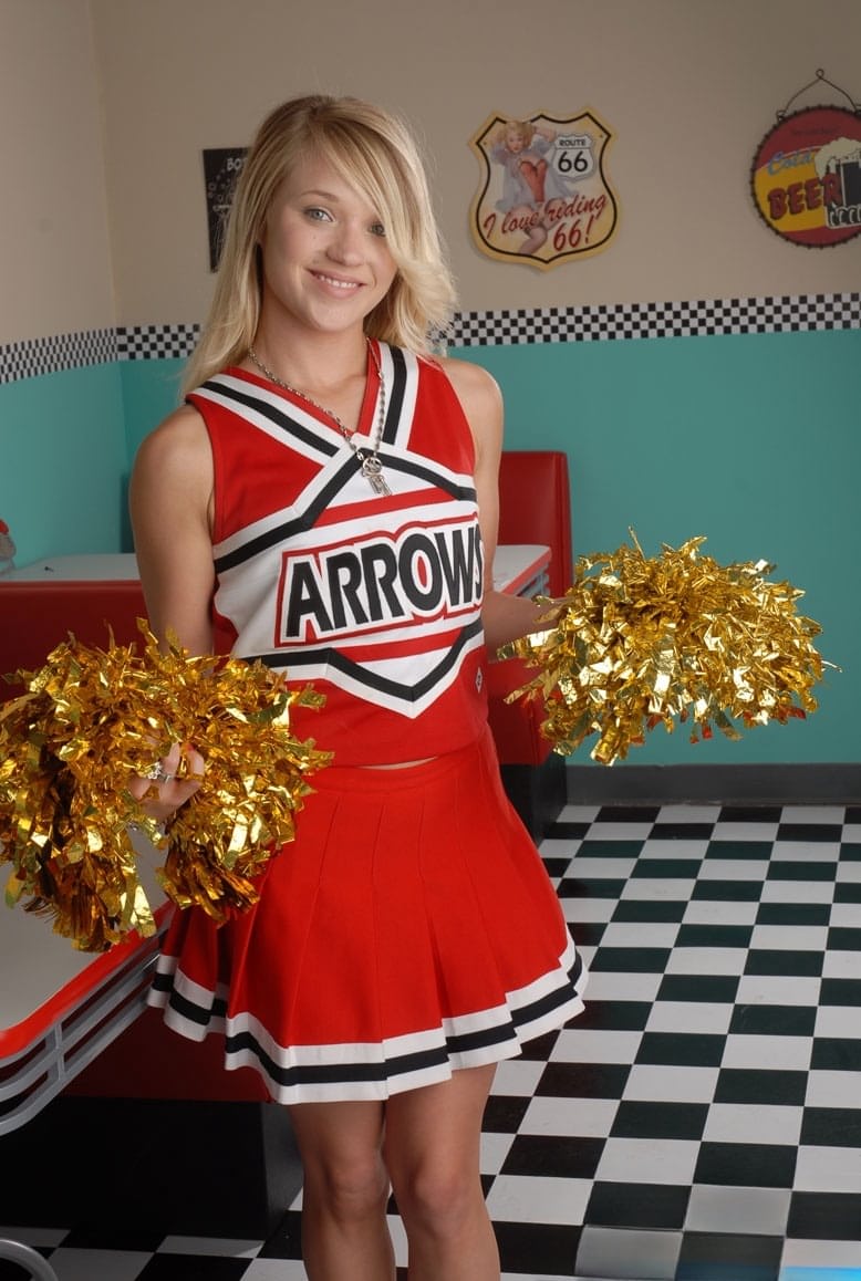 Cute college blonde Tegan Summers poses in a cheerleader outfit at a diner